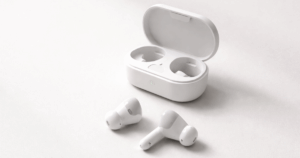 Minimal flat-lay of white wireless earbuds with an open charging case on a light gray, off-white gradient surface, softly lit with ample negative space, conveying affordable everyday tech.