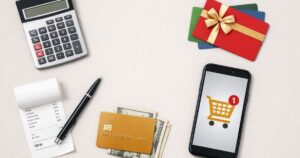 Minimal flat-lay of shopping essentials including a calculator, discounted gift cards, credit card with cash, receipt, and a smartphone showing an online shopping cart, representing smart shopping strategies and savings at checkout.